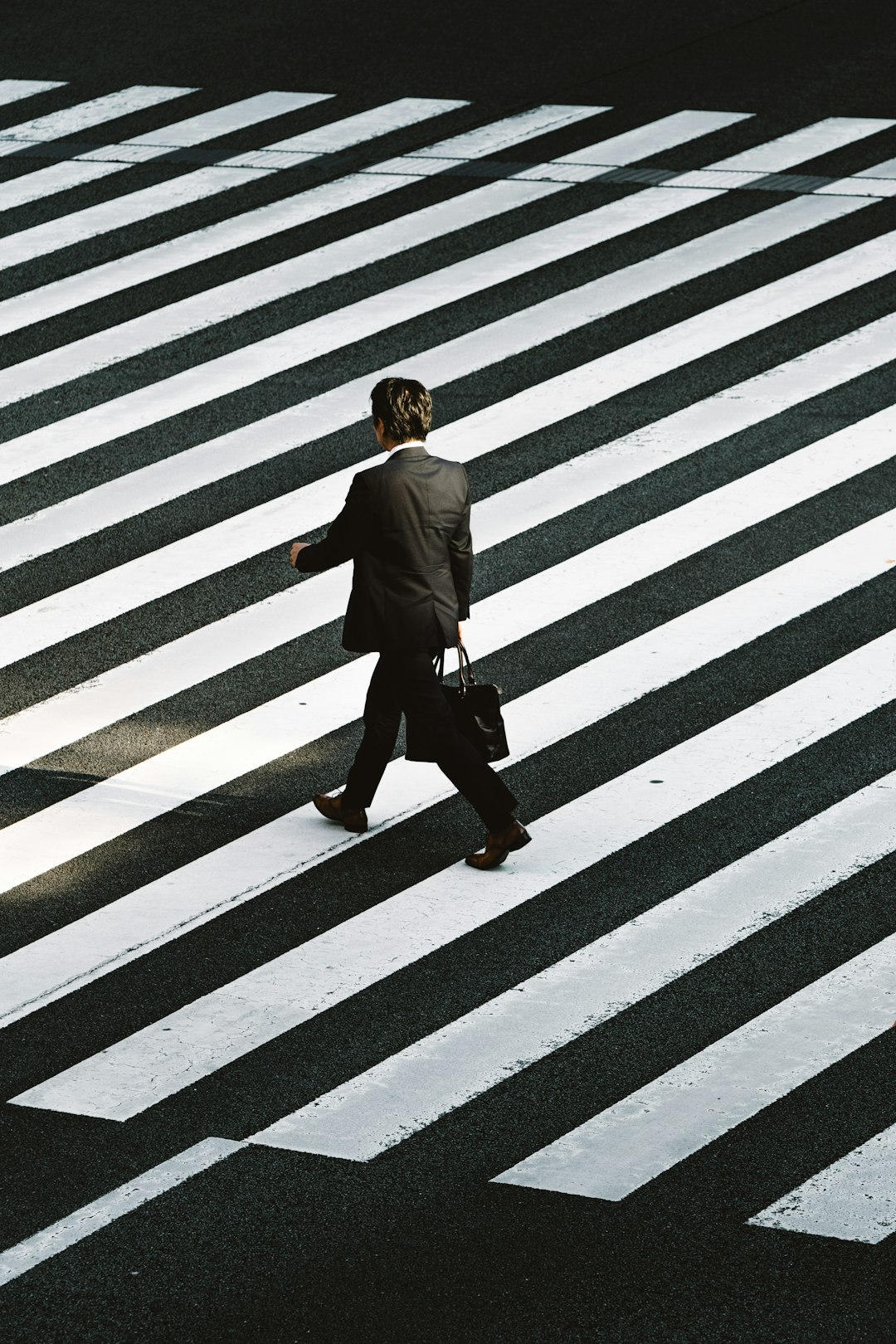 man-in-black-formal-suit-jacket-and-pants-carrying-black-bag-while-walking-on-pedestrian-lane-during-daytime-wuzjnov7t0g